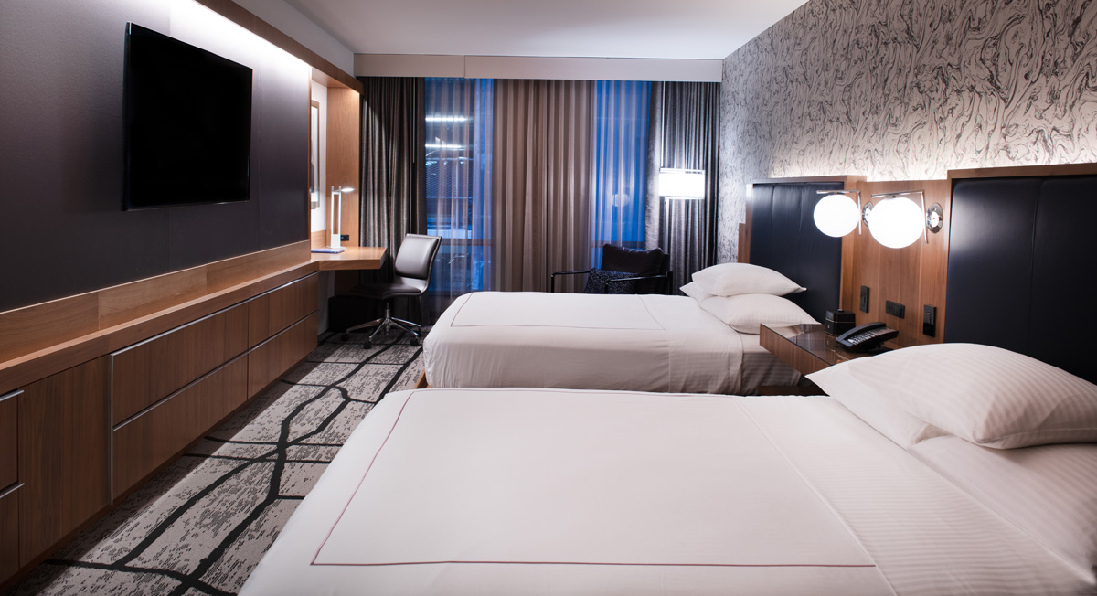 A hotel room with two double beds, a desk, and a TV on the wall.