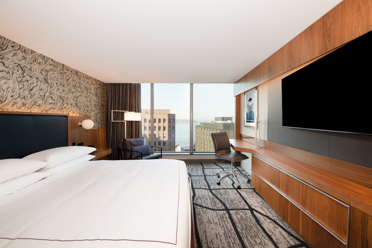 A hotel room with a large bed, desk, chair, and TV