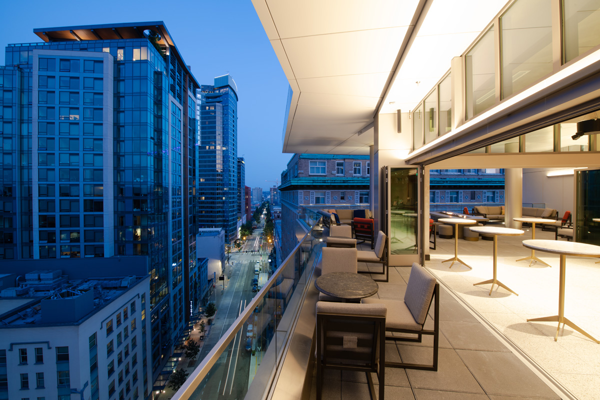 A balcony with furniture and a city view at dusk.